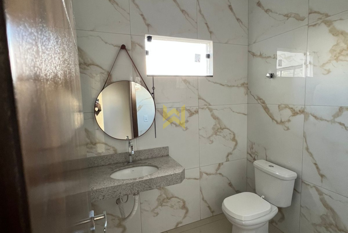 Banheiro moderno em imóvel à venda em Vilhena - RO, com revestimento em porcelanato marmorizado, pia de granito, espelho redondo e vaso sanitário branco.