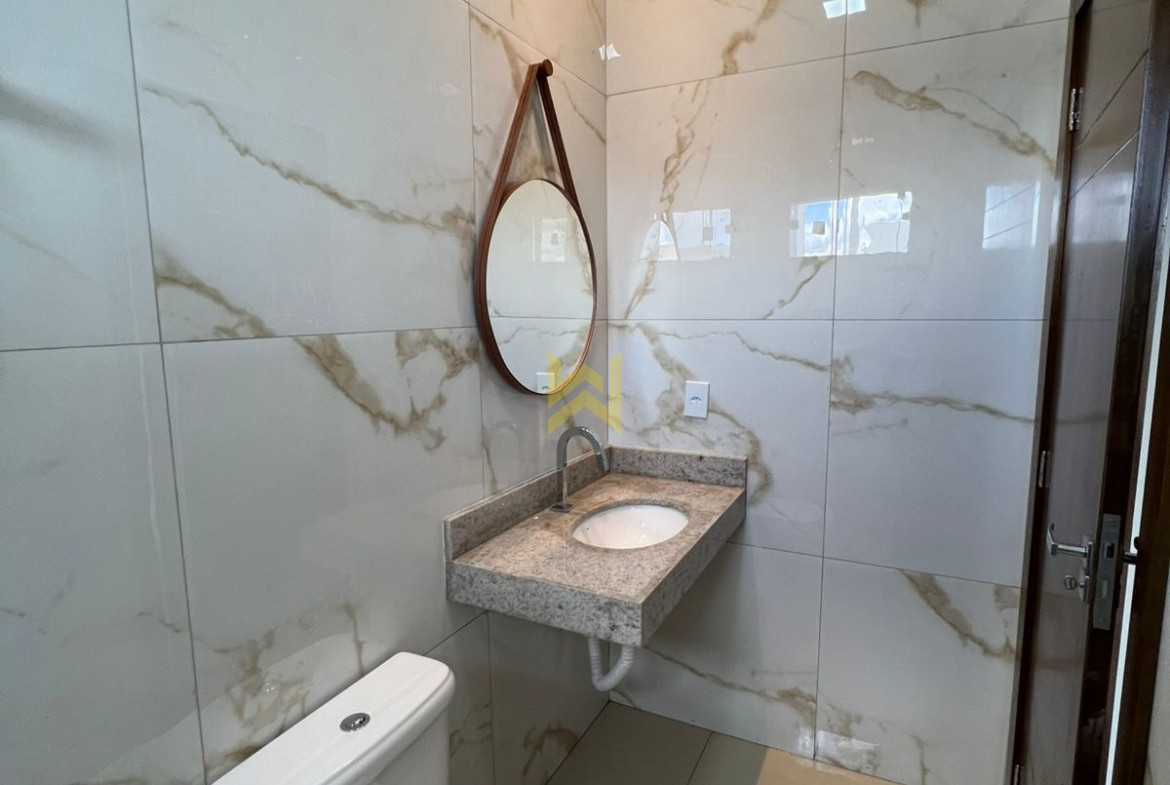 Banheiro moderno em imóvel à venda em Vilhena - RO, com revestimento em porcelanato marmorizado, pia de granito, espelho redondo e vaso sanitário branco.